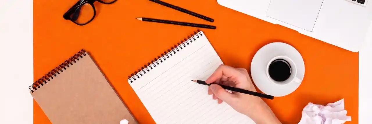 Leerer Notizblock mit Stift, Laptop und Kaffee auf orangefarbenem Papier