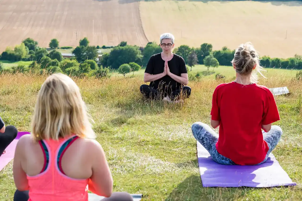 Yoga-Gruppe sitzt im Freien auf Matten auf einer Wiese